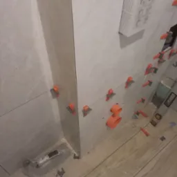 Układanie jasnych płytek w łazience w Katowicach, widoczne narzędzia glazurnicze i system poziomowania płytek.