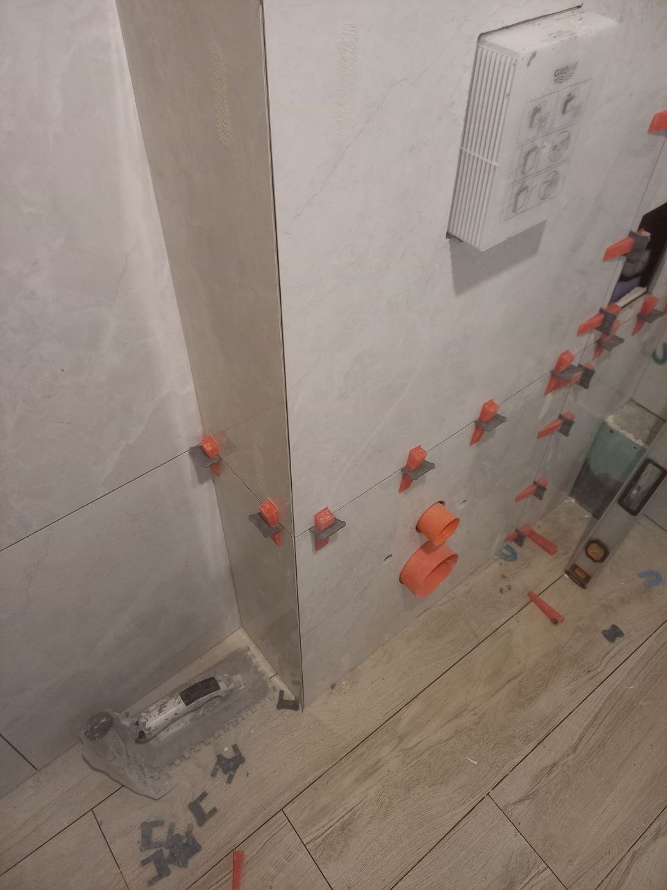 Układanie jasnych płytek w łazience w Katowicach, widoczne narzędzia glazurnicze i system poziomowania płytek.