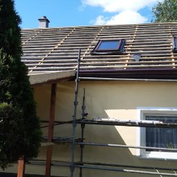 Usługi Dekarsko - Ciesielskie Grzegorz Lubowiecki - Dom jednorodzinny w trakcie przygotowania do położenia nowego pokrycia dachowego, widoczne łaty, okno dachowe i komin na tle błękitnego nieba z chmurami.