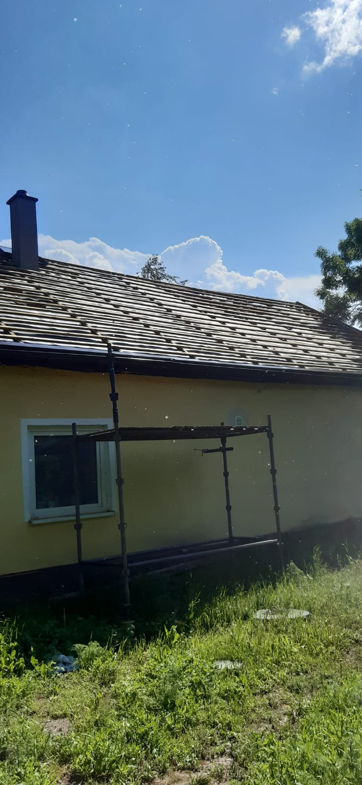 Żółty dom z nowym dachem z dachówki ceramicznej, widoczne rusztowanie i komin, błękitne niebo z chmurami w tle.