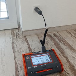 Skrobak Jan - Miernik Sonel MPI-540 podłączony do gniazdka elektrycznego, wyświetlający wartość impedancji pętli zwarcia ZL-PE = 0,82 Ω, na podłodze z paneli imitujących drewno.