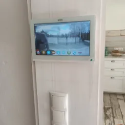 Zamontowany wideodomofon marki Eura z widokiem na bramę i zaparkowany samochód dostawczy, obok potrójny włącznik światła na pomalowanej na biało ścianie.