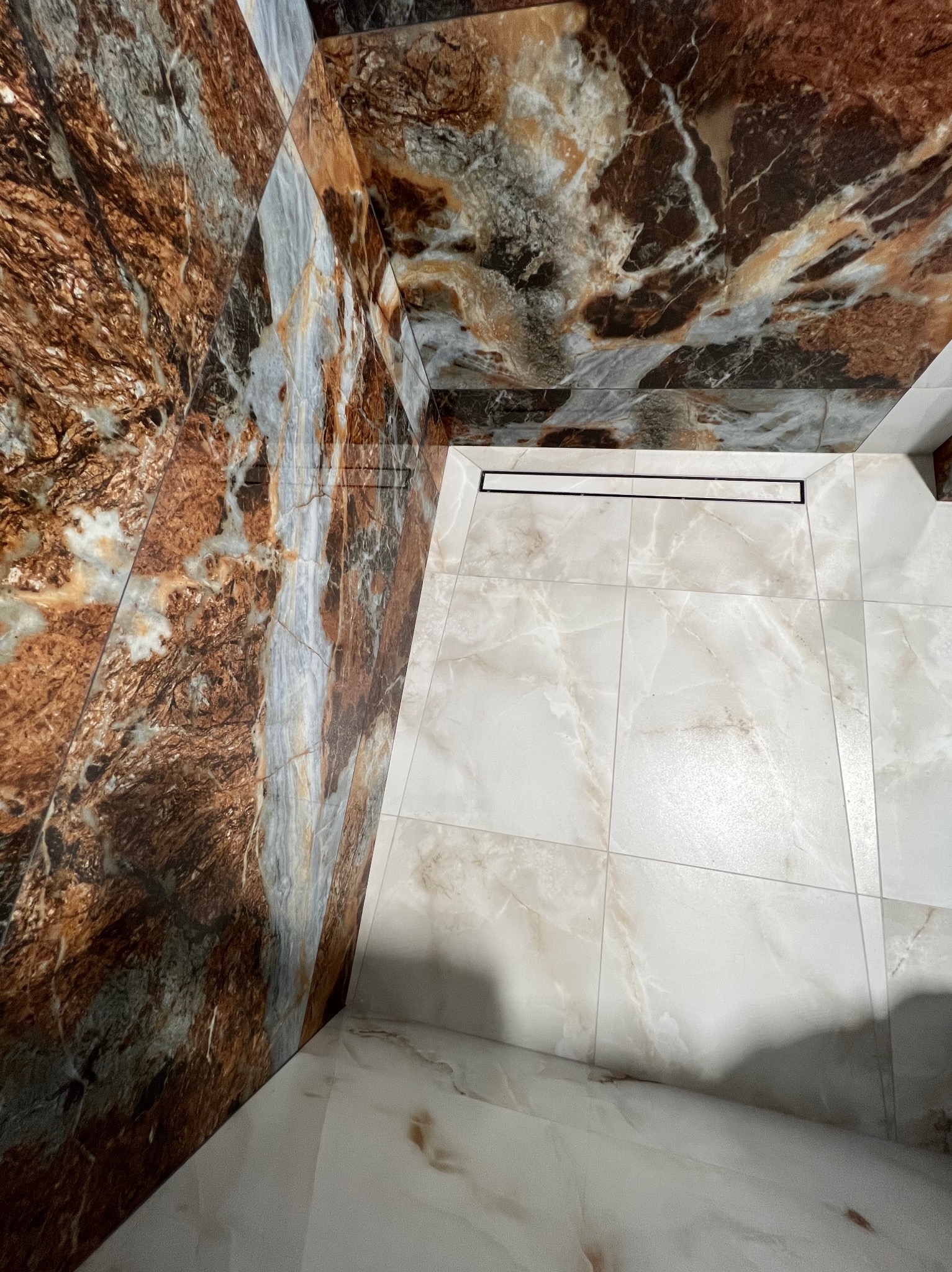 Wykończona łazienka z brązowo-białymi płytkami imitującymi marmur na ścianach i podłodze. Widoczny odpływ liniowy.