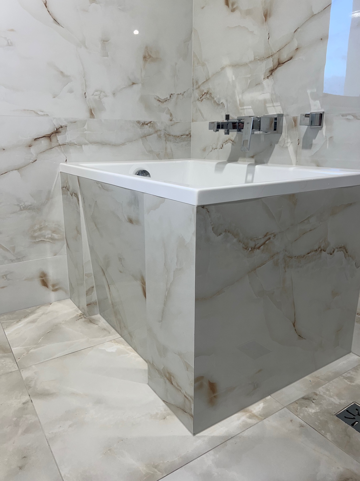 Wykończona łazienka: wanna obudowana płytkami imitującymi marmur, armatura chromowana, płytki podłogowe i ścienne w tym samym wzorze.