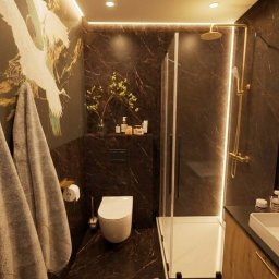 MICHAŁ WIĘCKOWSKI - PROJEKTOWANIE WNĘTRZ - Elegancka łazienka z kabiną prysznicową, marmurowymi ścianami i akcentami złota. Na ścianie widoczny motyw żurawi i wiszące ręczniki.