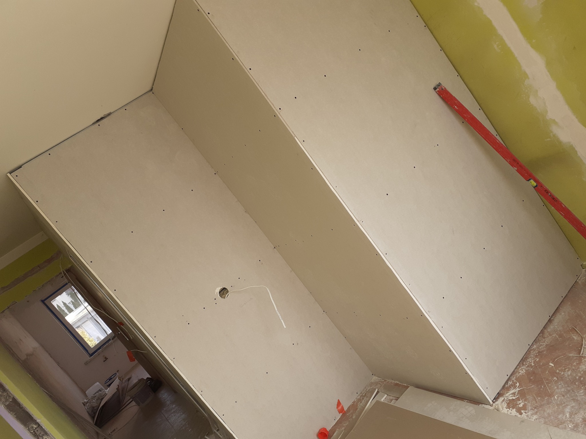 Montaż płyt gipsowo-kartonowych na poddaszu, widoczny poziomica, otwór na instalację elektryczną i fragment okna w tle.