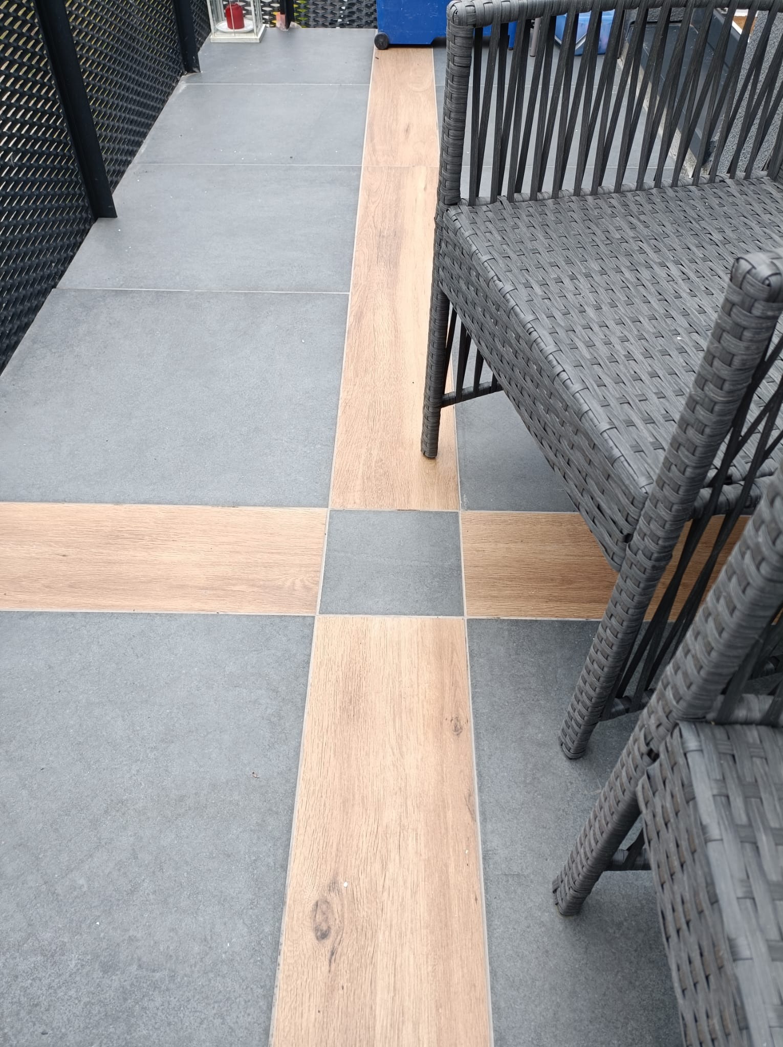 Szare płytki podłogowe z drewnopodobnymi wstawkami ułożone w krzyżowy wzór, widoczne krzesła z tworzywa sztucznego.