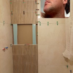 Mariusz Zaniewicz - Układanie płytek w łazience, widoczne płytki imitujące drewno, użyte klipsy poziomujące. Fragment rozmowy wideo w rogu ekranu. Prace w toku, widoczne niedokończone fragmenty.