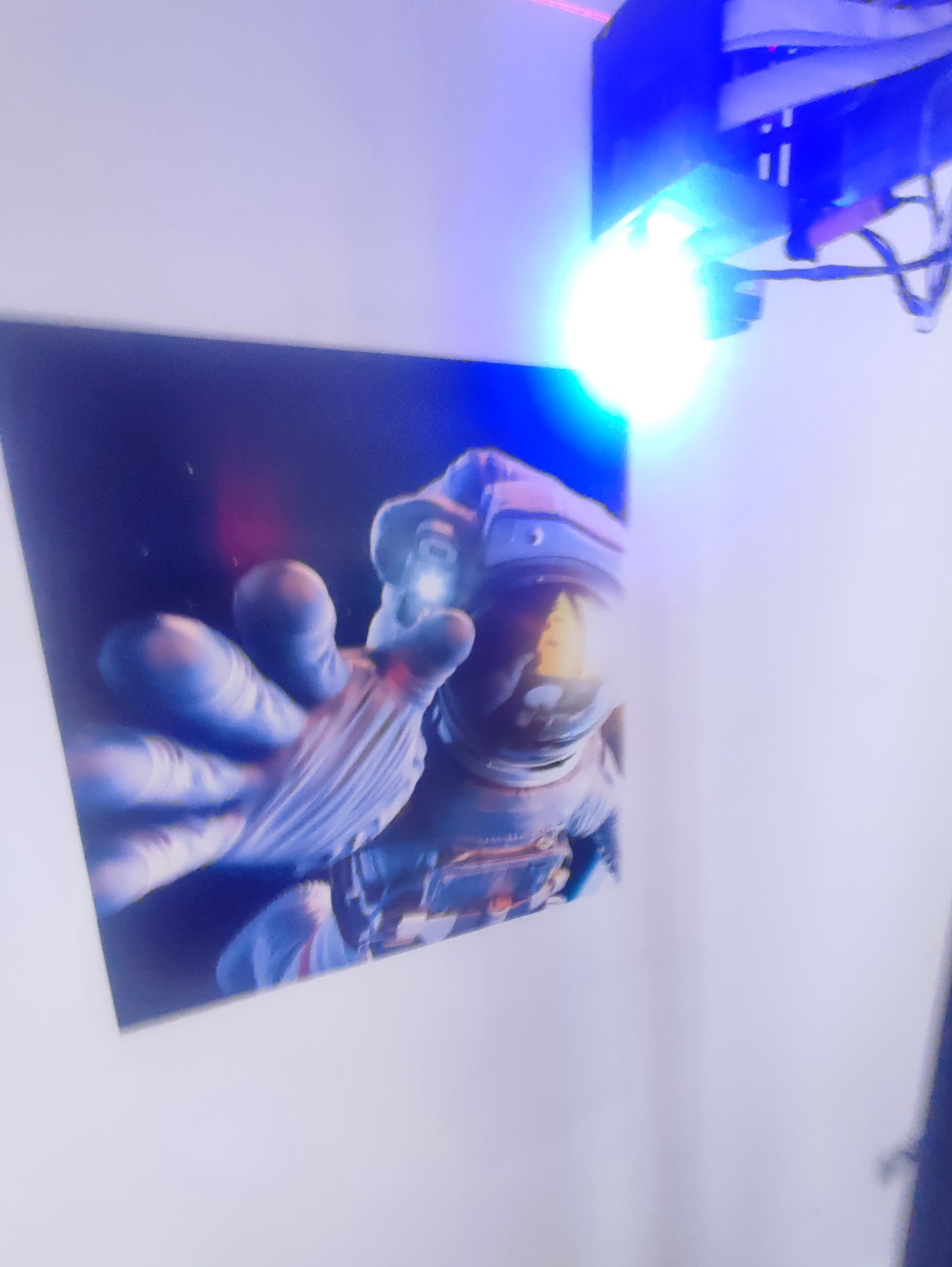 Zdjęcie wydrukowanego obrazu astronauty w kombinezonie, z wyciągniętą ręką, oświetlonego lampą biurkową.