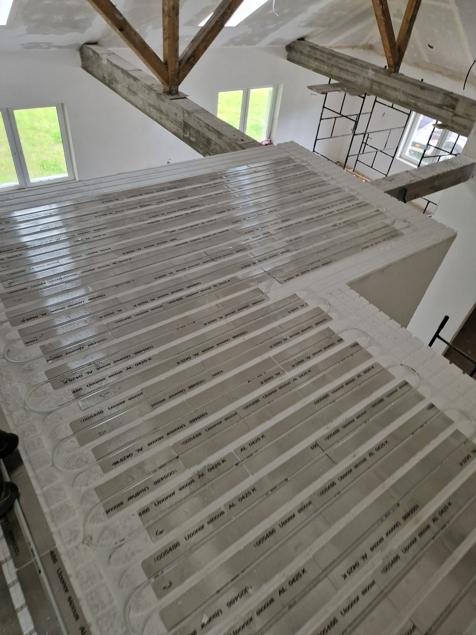 Instalacja ogrzewania podłogowego Upornor Siccus AL 0425 K na izolacji, widoczne elementy konstrukcyjne dachu i okna. Prace instalacyjne w trakcie realizacji.