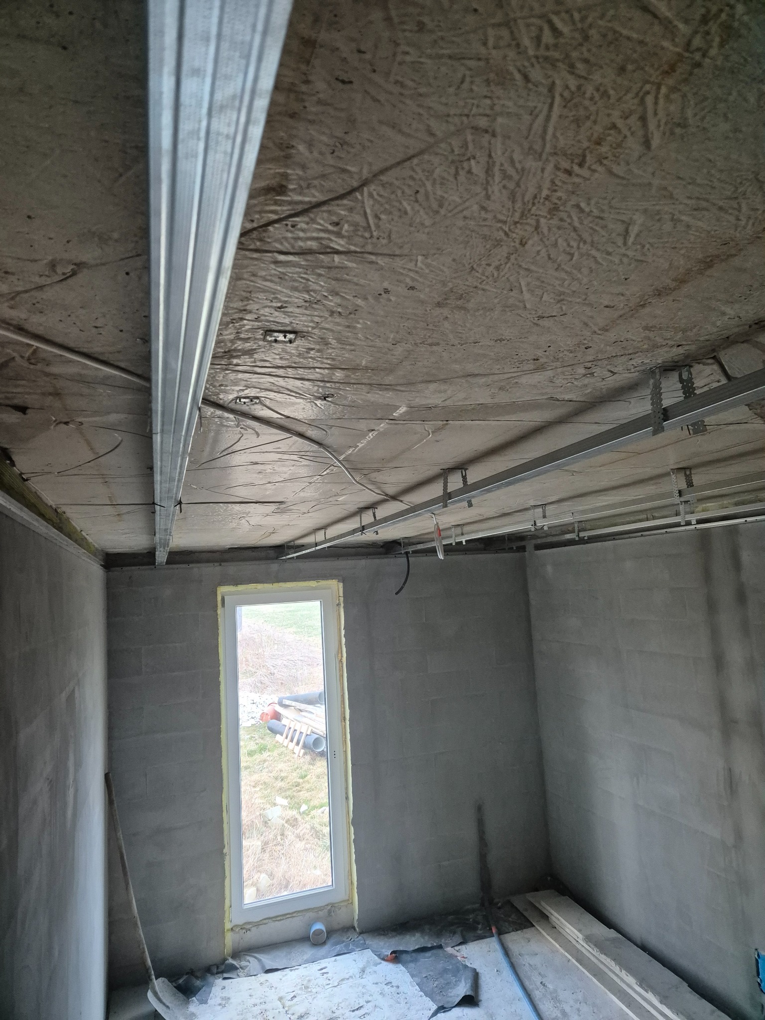 Montaż metalowej konstrukcji sufitu podwieszanego w surowym wnętrzu z widocznym oknem i narzędziami.