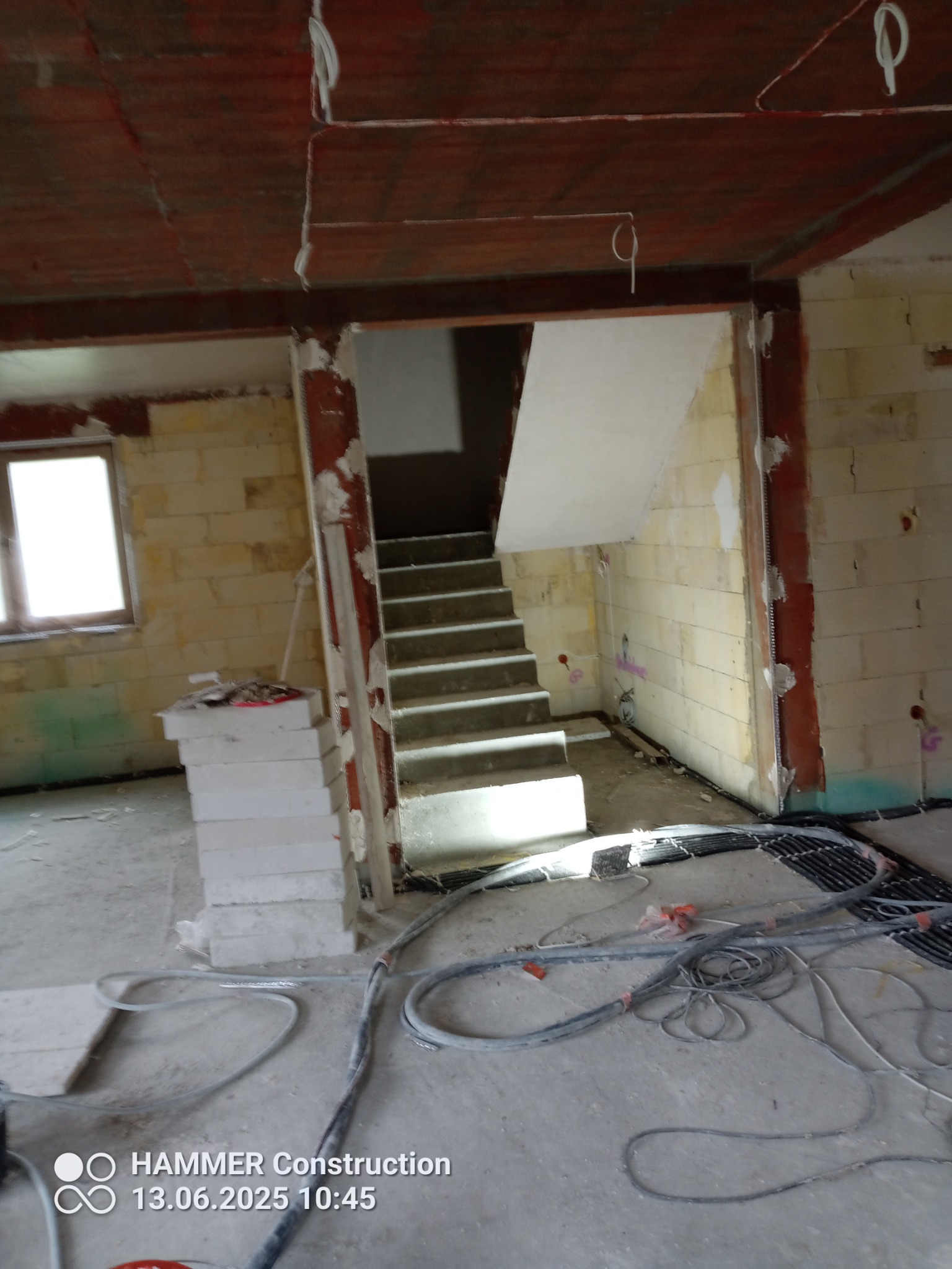 Wnętrze w trakcie prac wykończeniowych: surowe ściany z bloczków, schody, widoczne przewody elektryczne i instalacje. Stan deweloperski, przygotowanie do dalszych prac.