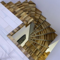 Mariusz Buja - Spiralne schody drewniane z mozaikową fakturą stopni, widok z góry, kontrastujące z białymi panelami podłogowymi i ścianami. Unikalny wzór i nowoczesny design.