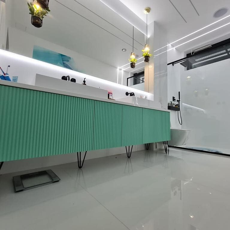 Nowoczesna łazienka z długą, miętową szafką pod umywalkę na czarnych nóżkach, oświetlona ledami i wiszącymi lampami z roślinami. Minimalistyczny design.