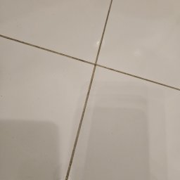 Tomasz Łuszczek - Białe płytki podłogowe z widocznymi, zabrudzonymi fugami w układzie krzyżowym. Perspektywa z góry, ukazująca detale zabrudzeń w spoinach.