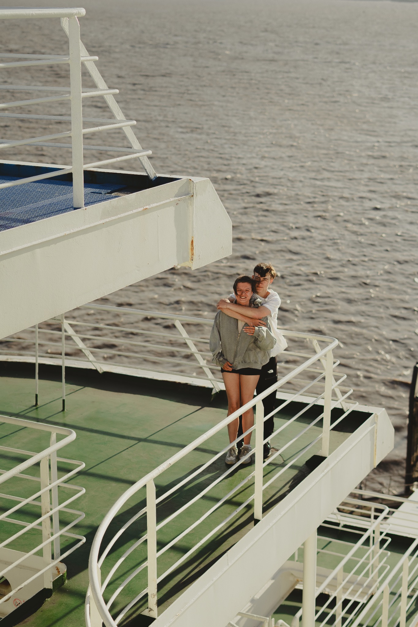 Para obejmująca się na pokładzie promu z widokiem na morze w tle.