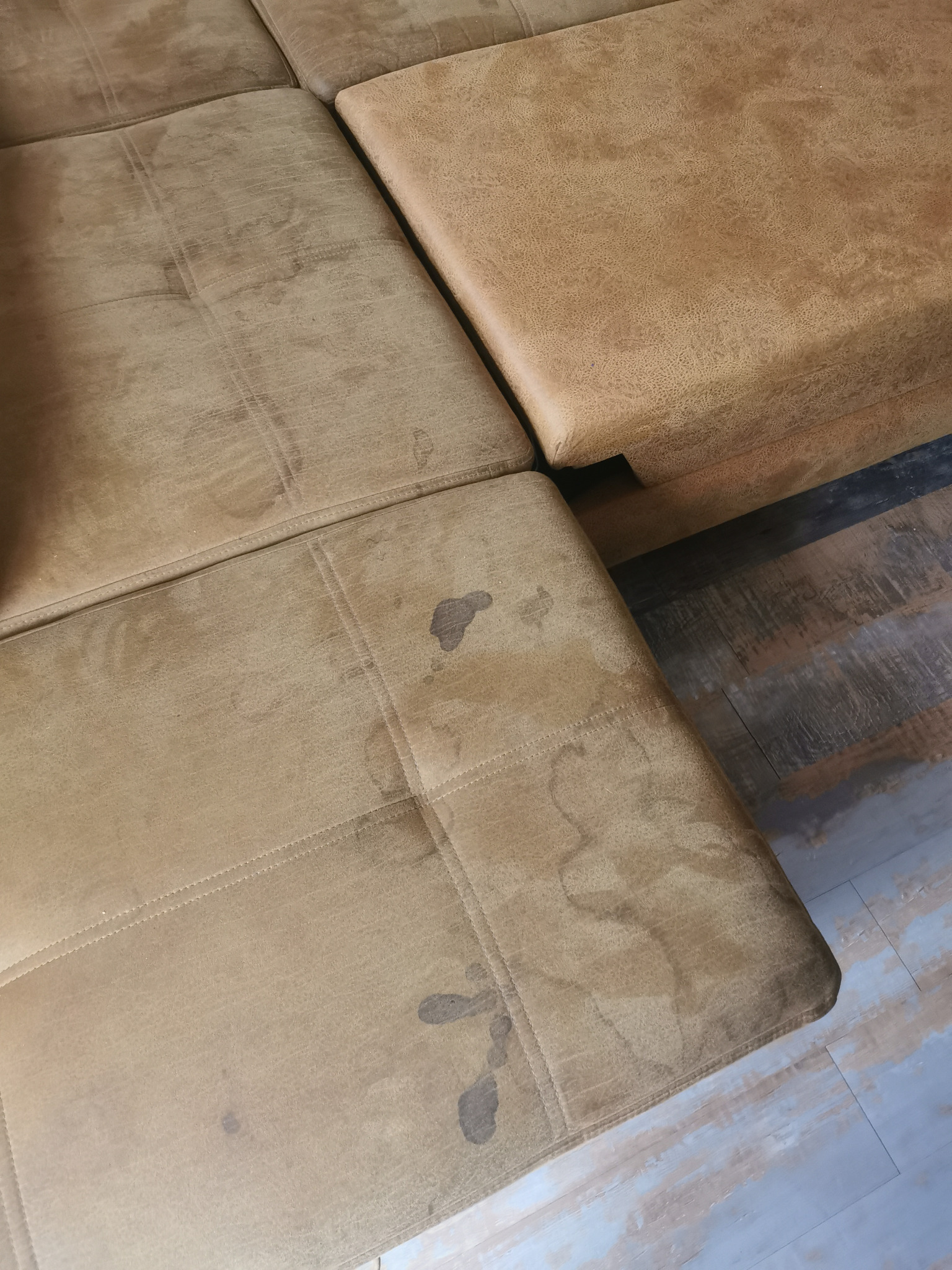 Fragment beżowej, modułowej kanapy z widocznymi plamami na siedzisku i oparciu, ukazujący potrzebę czyszczenia tapicerki.