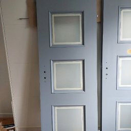 Perfect Tynk - Dwie szare, odnowione drzwi z trzema kwadratowymi przeszkleniami, zabezpieczonymi taśmą malarską. Widoczne ślady szpachli i przygotowania do malowania.