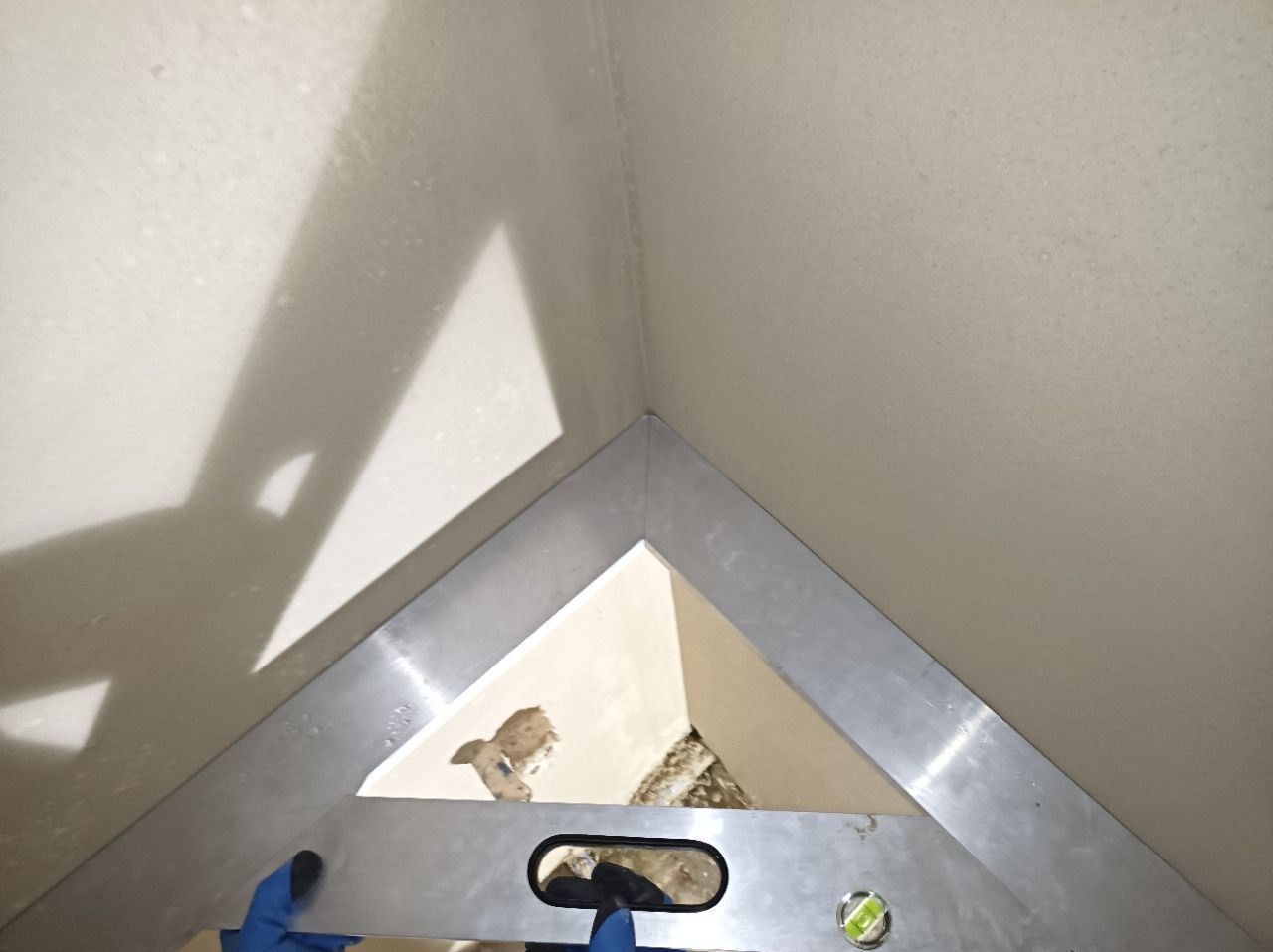 Przybliżenie kąta ściany w trakcie prac wykończeniowych, z widocznym aluminiowym kątownikiem i fragmentami starego tynku.