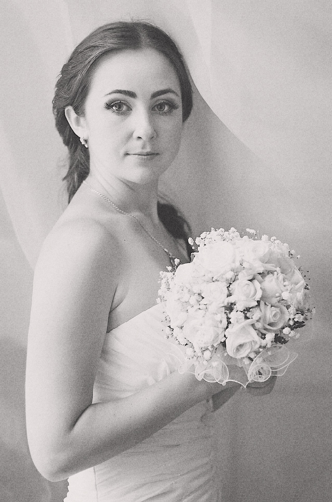 Portret panny młodej w monochromatycznej tonacji, subtelnie trzymającej bukiet białych róż i gipsówki, z delikatnym welonem w tle.