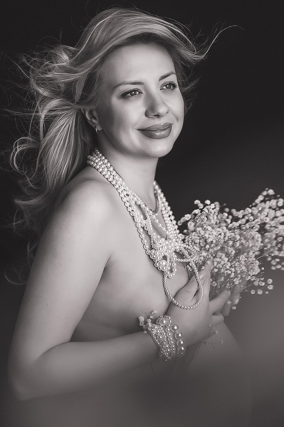Czarno-białe, artystyczne ujęcie kobiety z perłami i gipsówką na ciemnym tle. Sesja w Lublinie, podkreślająca naturalne piękno i subtelność.