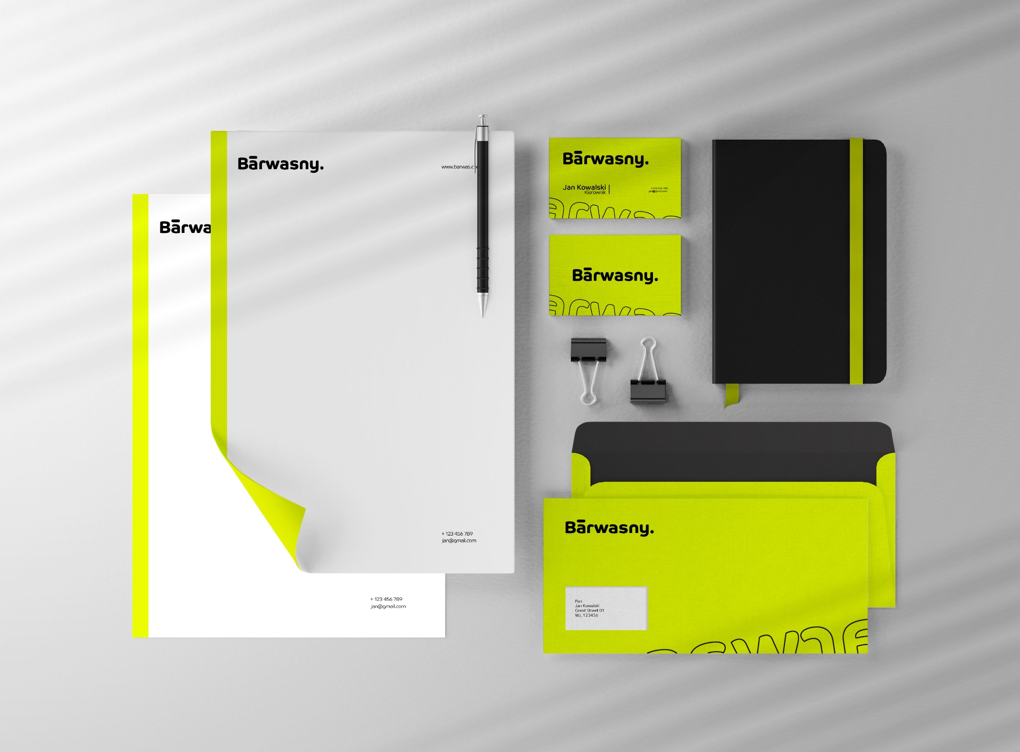 Zestaw identyfikacji wizualnej firmy z logo w kolorze limonkowym, zawierający papier firmowy, wizytówki, notes, koperty i długopis na jasnoszarym tle.