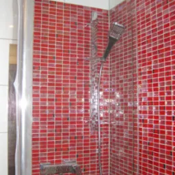 Kabina prysznicowa z czerwoną mozaiką, chromowana armatura i deszczownica, widoczne ślady wody na szkle.