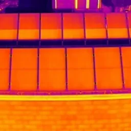 Termowizyjne zdjęcie paneli fotowoltaicznych na dachu budynku, ukazujące zacienione moduły i aktywne diody bocznikujące, z wyraźnym kontrastem temperatur.