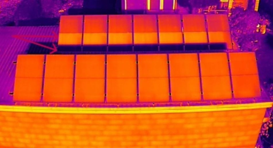 Termowizyjne zdjęcie paneli fotowoltaicznych na dachu budynku, ukazujące zacienione moduły i aktywne diody bocznikujące, z wyraźnym kontrastem temperatur.