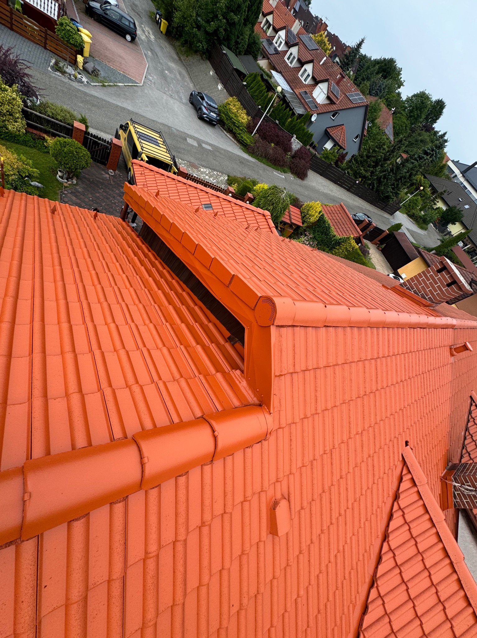Pomarańczowy dach z ceramicznej dachówki po renowacji, widok z góry na tle zabudowy jednorodzinnej i ulicy.