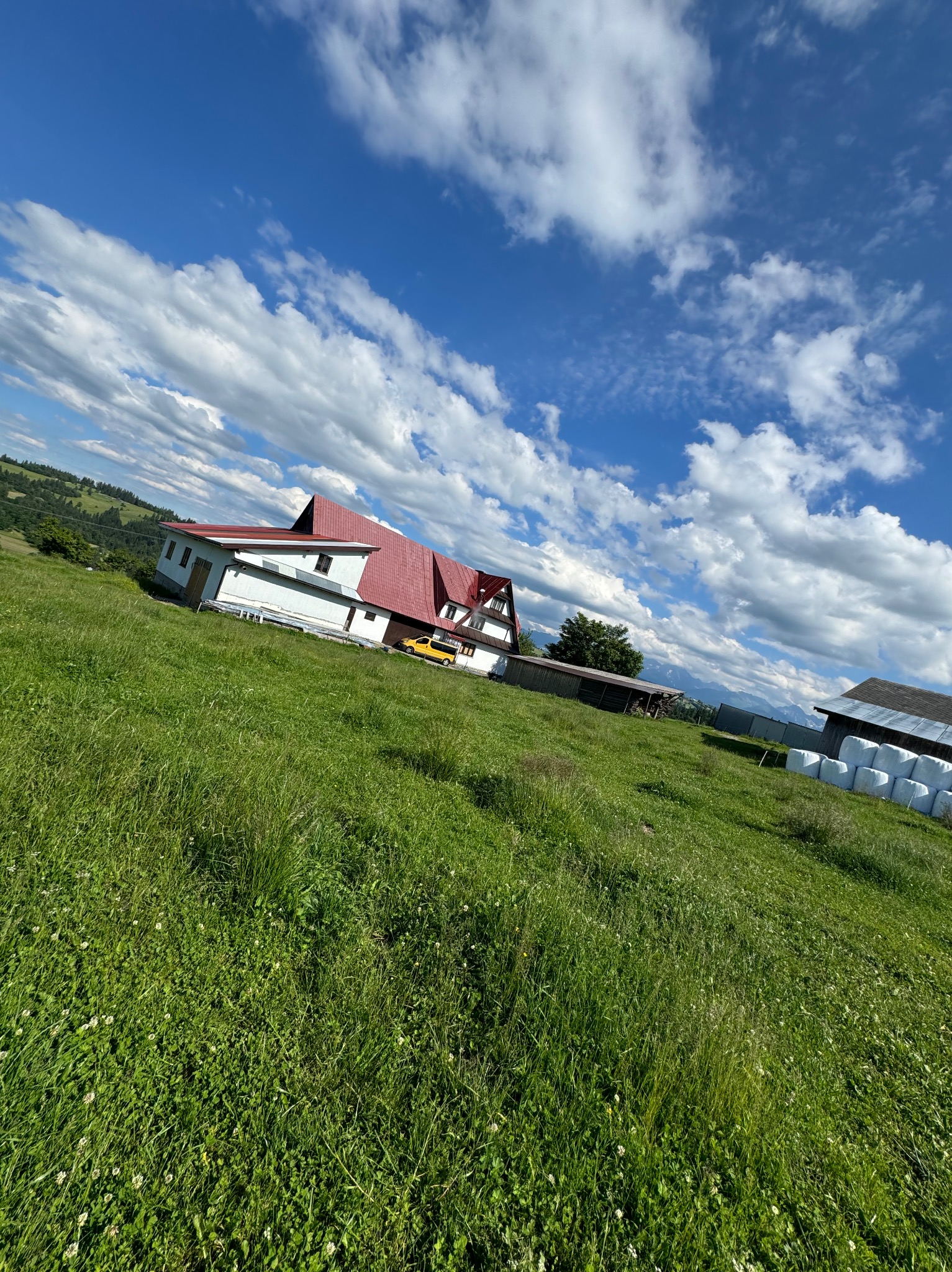 Dom z czerwonym dachem na zielonym wzgórzu, błękitne niebo z obłokami w tle.