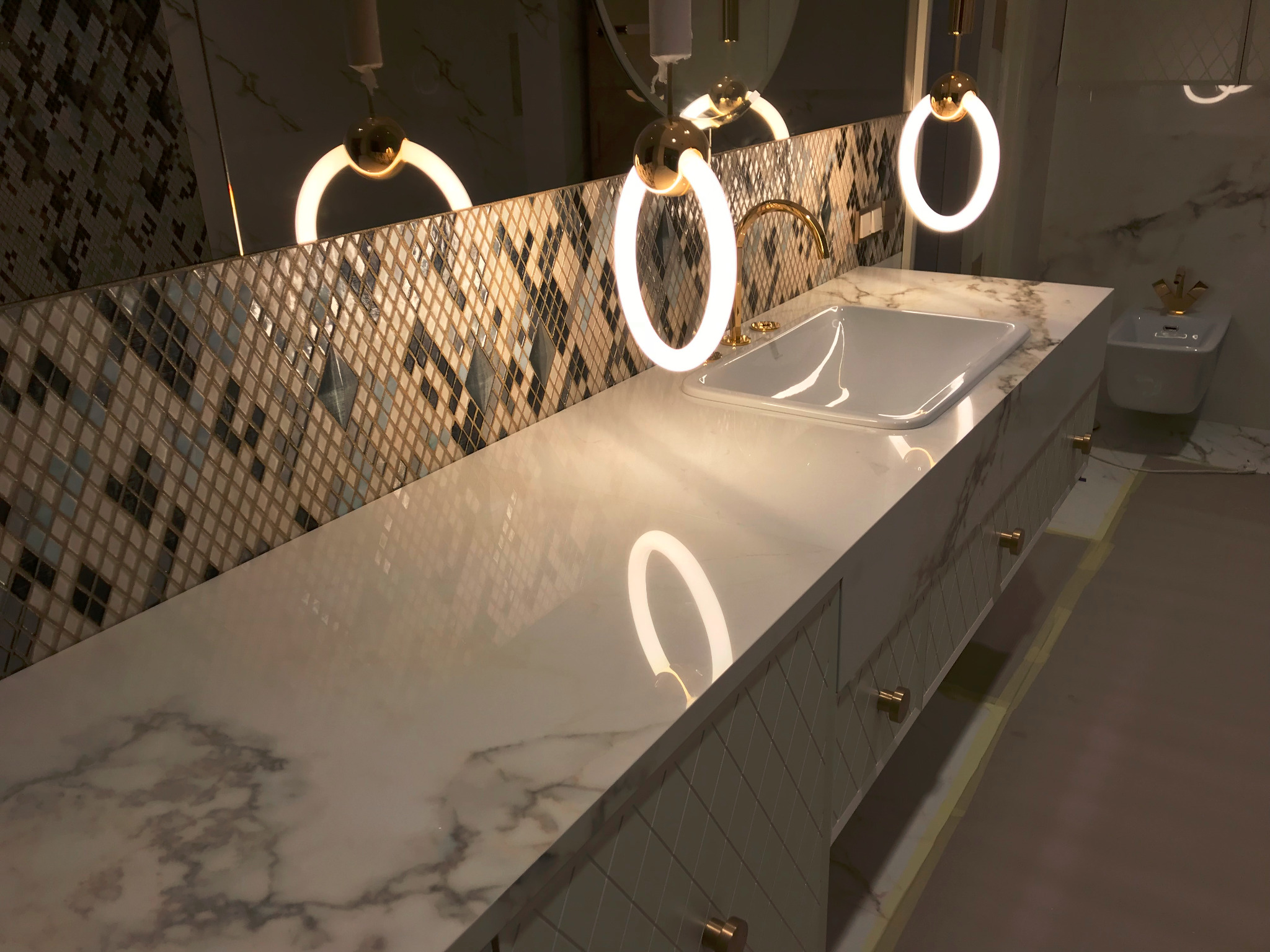 Biały blat z marmuru z umywalką w łazience z mozaikową ścianą i okrągłymi lampami LED