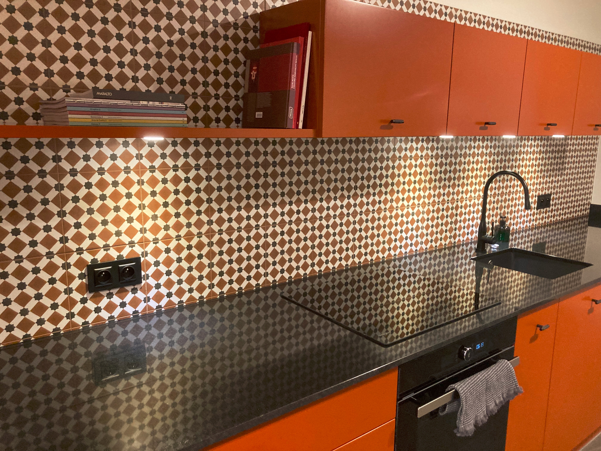 Nowoczesna kuchnia w Gdańsku z pomarańczowymi szafkami, czarnym blatem i dekoracyjną mozaiką na ścianie.