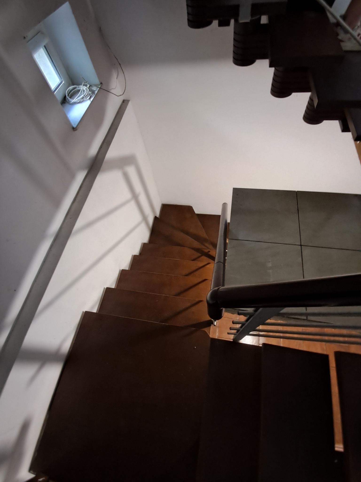 Wysoki kąt widzenia na drewniane schody z metalową barierką i małym oknem z kablami na ścianie.