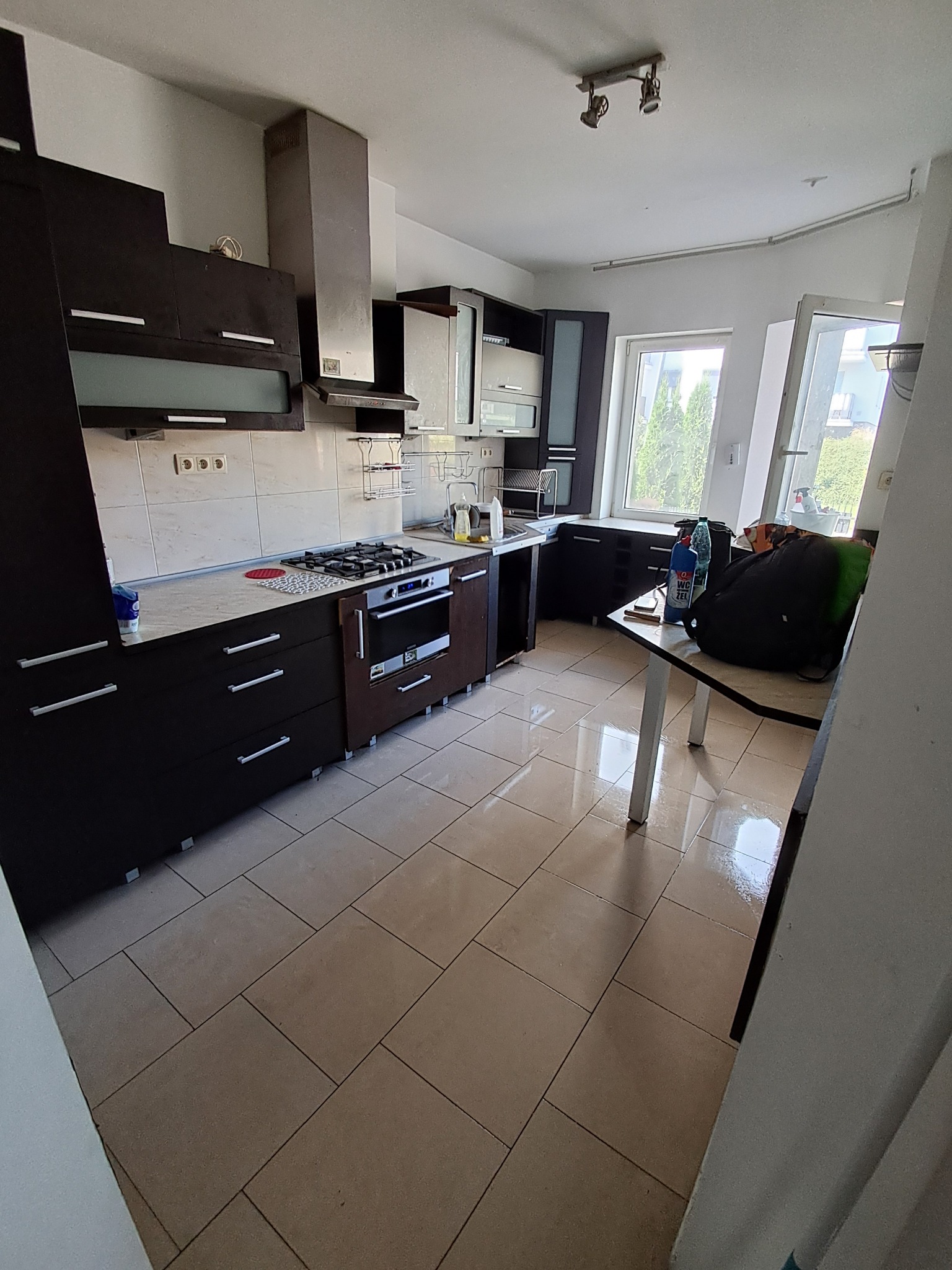 Kuchnia z ciemnymi meblami przed sprzątaniem, widoczny bałagan na stole i butelka środka czyszczącego WC Żel.