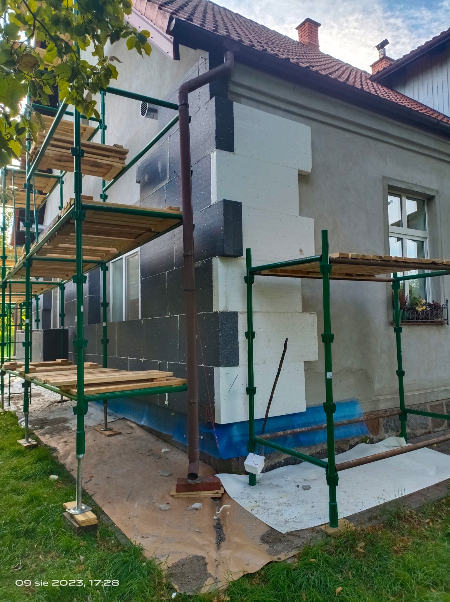 Ocieplanie elewacji domu jednorodzinnego z użyciem styropianu grafitowego i białego, widoczne rusztowanie i przygotowane podłoże.