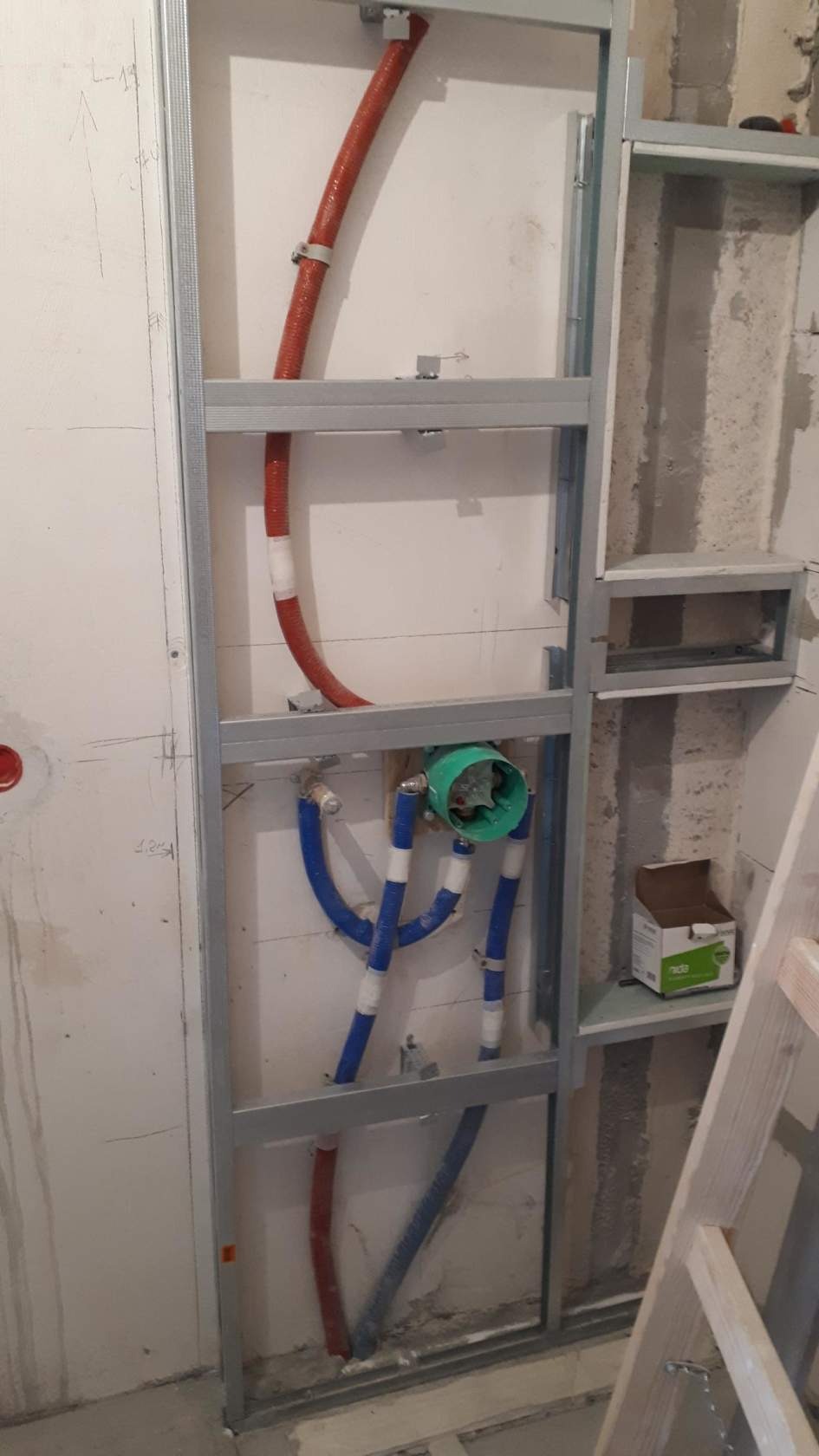Stelaż pod zabudowę z płyt karton-gips, widoczne rury instalacji wodnej w izolacji oraz puszka pod baterię, w tle fragment drabiny.
