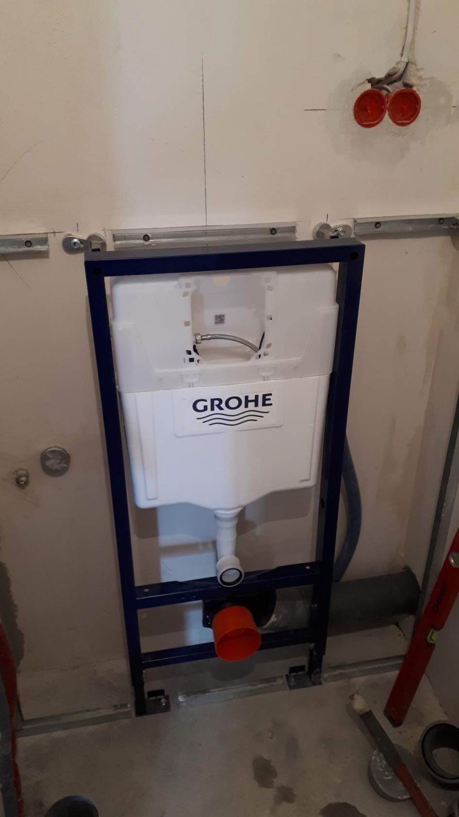 Stelaż podtynkowy Grohe zamontowany na metalowej ramie, widoczne instalacje wodno-kanalizacyjne i elektryczne w surowej łazience przed wykończeniem.