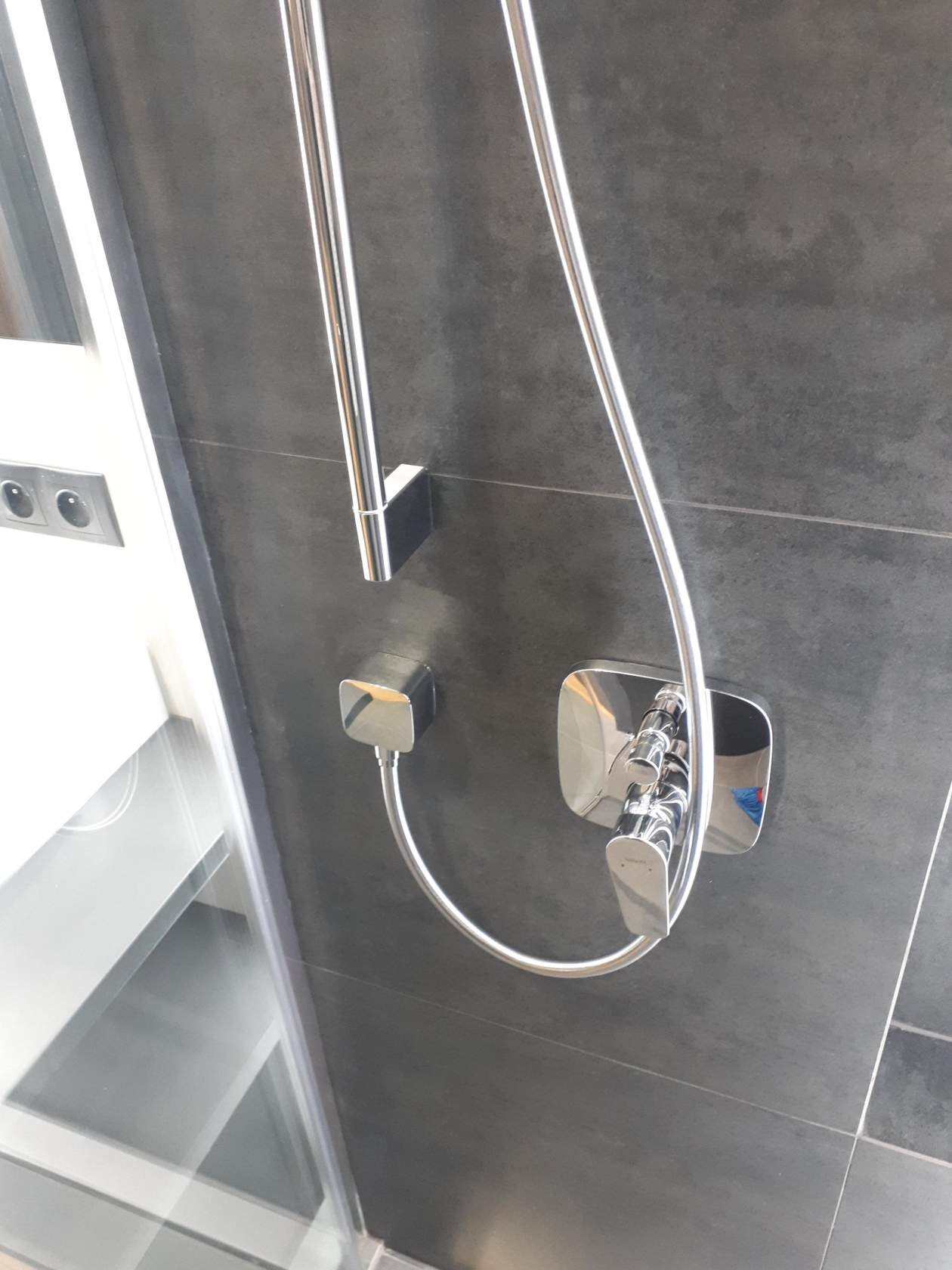 Bateria prysznicowa z termostatem, chromowana, zamontowana na ciemnoszarych płytkach w kabinie prysznicowej, widoczny fragment instalacji elektrycznej.