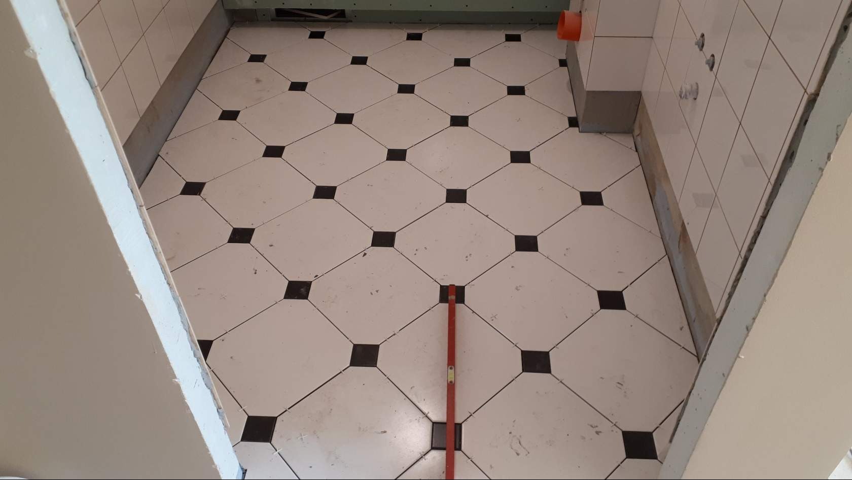 Układanie podłogi z białych i czarnych płytek w romby, poziomica na podłodze, widok na ściany w trakcie prac w Krakowie.