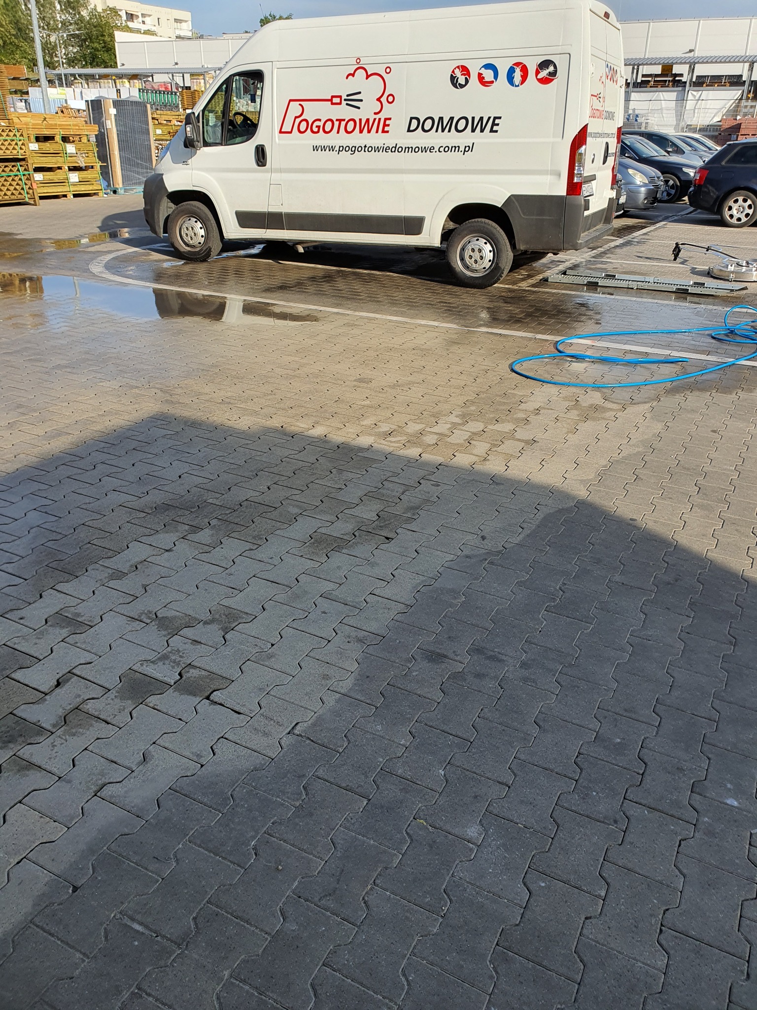 Czyszczenie kostki brukowej przy użyciu profesjonalnego sprzętu i samochodu firmowego z logo Pogotowie Domowe. Widoczna różnica między umytą a brudną powierzchnią.