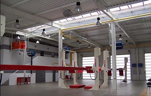 Wnętrze przestronnego warsztatu samochodowego w Mikołowie z kilkoma podnośnikami kolumnowymi, widoczne oświetlenie przemysłowe i fragmenty instalacji. Na ścianach białe płytki. Czysta posadzka.