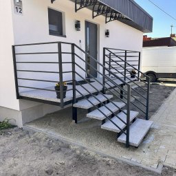 MATEUSZ BARAŃSKI KREWICUSTOM - Zewnętrzne schody z szarego granitu z czarną, poziomą balustradą, prowadzące do wejścia domu z numerem 12. Widoczne donice z kwiatami i częściowo zaparkowany biały bus.