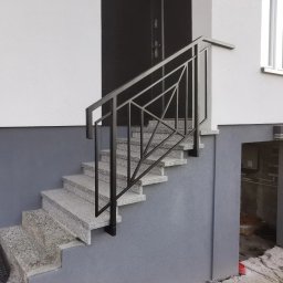 MATEUSZ BARAŃSKI KREWICUSTOM - Zewnętrzne schody z szarego granitu z nowoczesną, geometryczną balustradą z czarnego metalu. Minimalistyczny design, jasna elewacja budynku w tle.