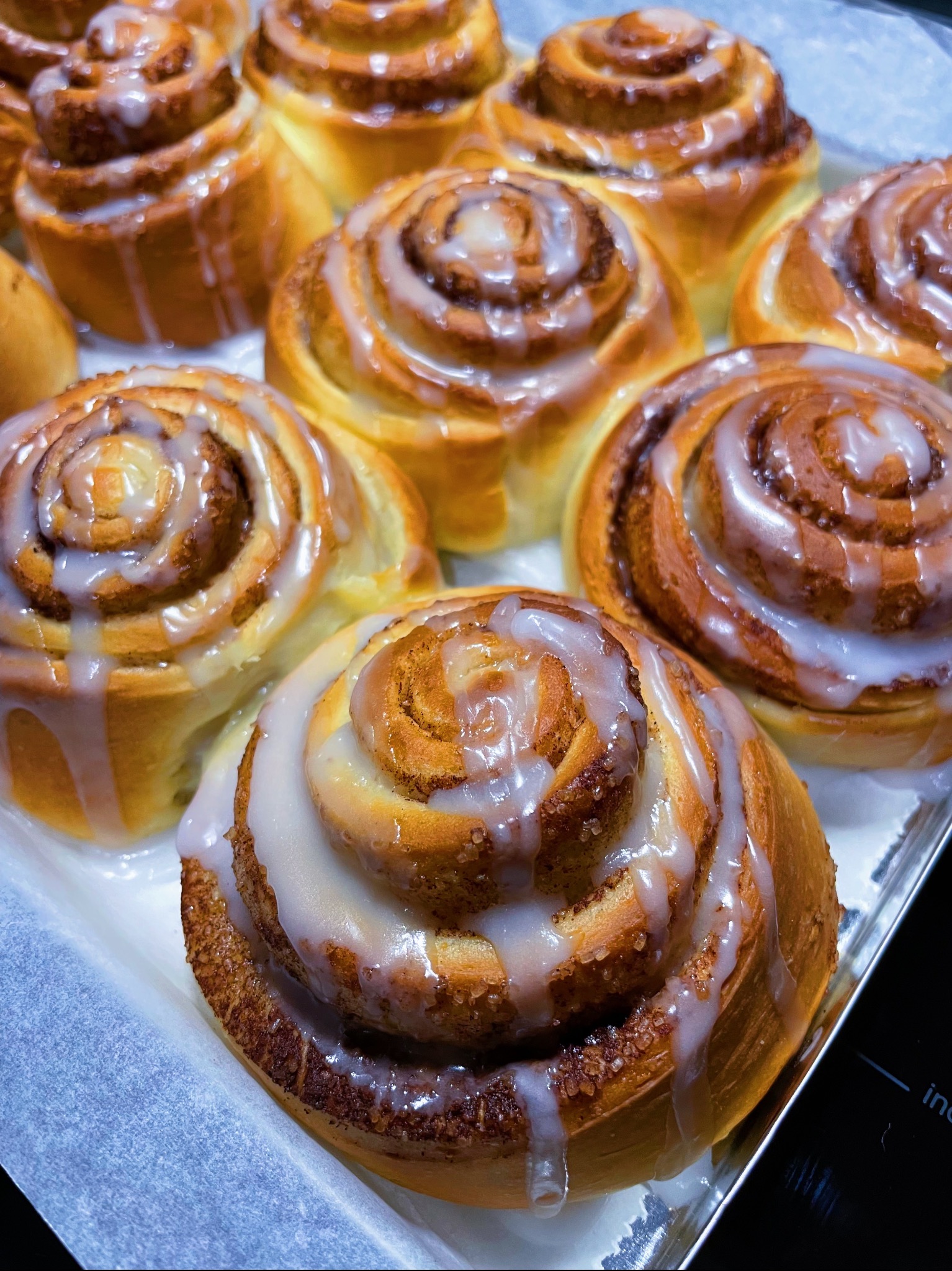 Świeżo upieczone cynamonki na blasze, polane lukrem, z widoczną strukturą ciasta i kryształkami cukru.