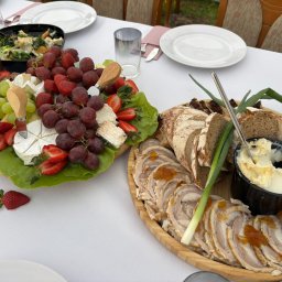 P.H.U. Filip Zając - Elegancko podane deski z serami, owocami i wędlinami na białym obrusie, z zielonymi dodatkami. Widoczne naczynia i szklanki, sugerujące gotowość do spożycia.