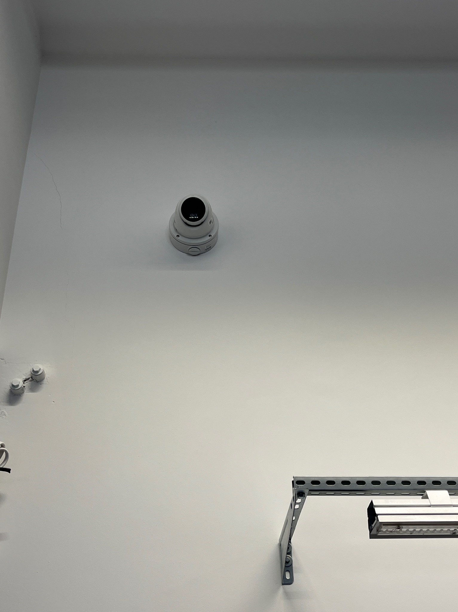 Kopułkowa kamera monitoringu zamontowana na białym suficie, widoczna z dołu. Obok widoczne elementy instalacji oświetleniowej.