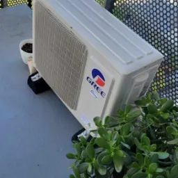 Klimatyzator marki Gree zamontowany na balkonie w Krakowie, widoczny przez ażurową balustradę, obok doniczka z kwiatami.