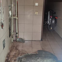 Clean - Podłoga po remoncie z widocznymi śladami kleju, resztkami płytek i mopem przy rurach, rower w tle.