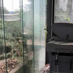 Zabrudzone, szklane panele przesuwne tarasu z widocznymi smugami i zaciekami, obok grill na kółkach z akcesoriami, widok z zewnątrz.